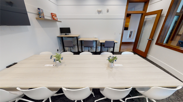 Conference room with large table, television, board games, and sit/stand desks on the side
